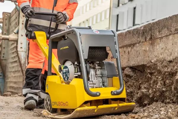 Plate compactor used on site to compact hardcore in an excavated trench during groundwork preparation.